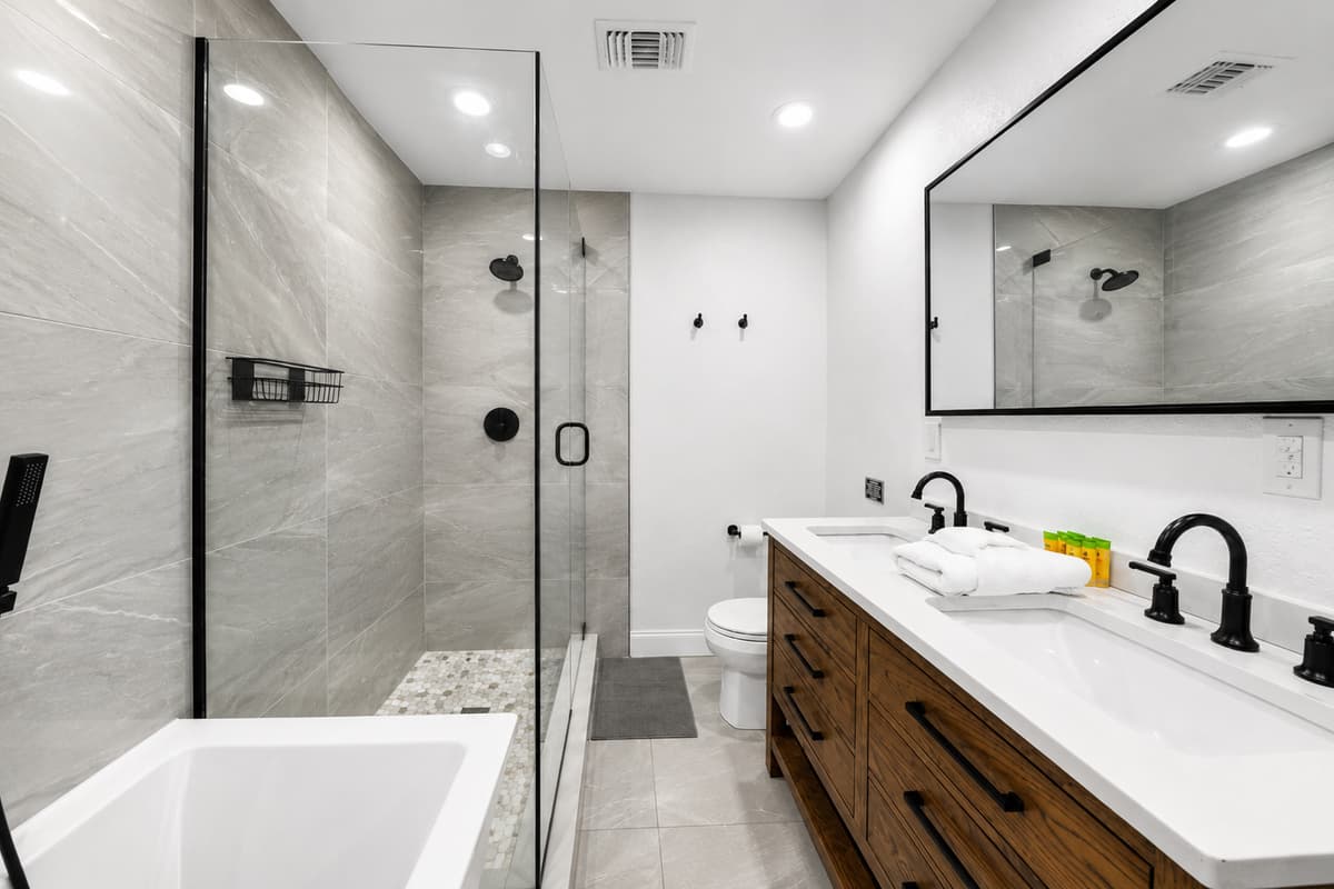 Modern spa-style bathroom with dual sinks, wood vanity, frameless glass shower, and elegant tile finishes.