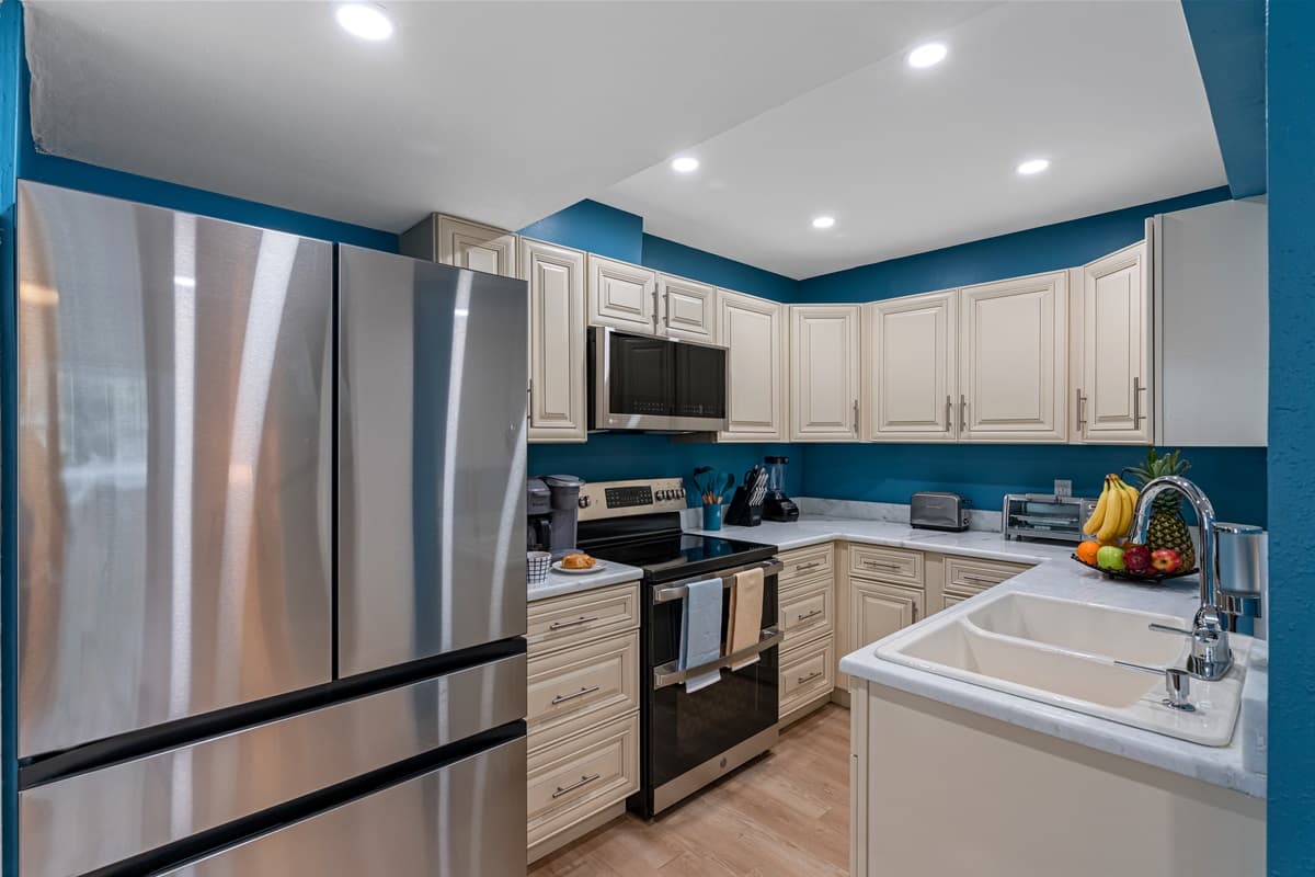 This kitchen is more than just a functional space; it's a culinary sanctuary that inspires creativity, fosters connection, and nourishes the soul. Huge fridge, white cupboards, blue painted walls, complete appliances, and well-stocked utensils.
