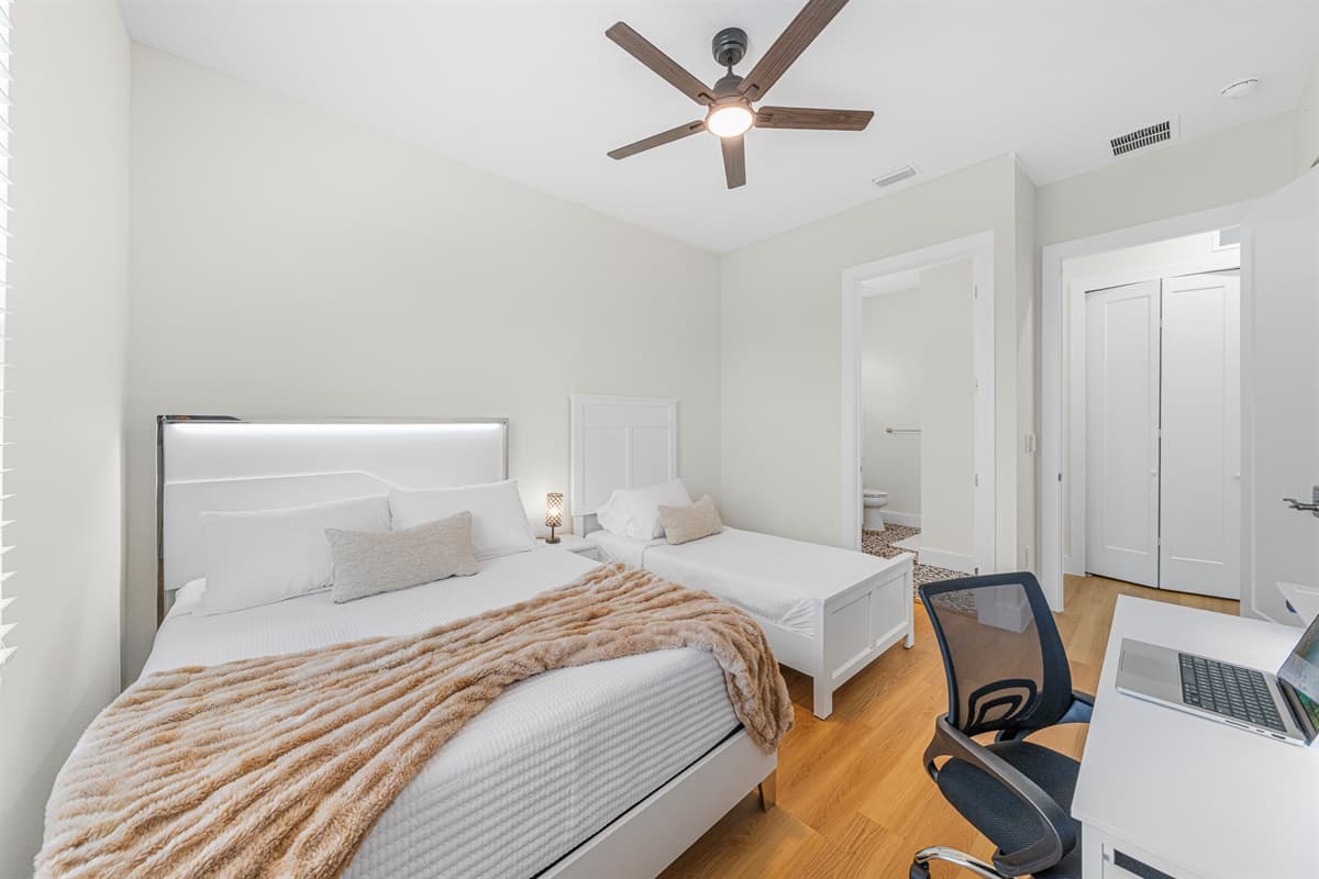 Comfortable and modern bedroom featuring a cozy bed, workspace desk, and convenient access to nearby rooms—perfect for both rest and productivity.