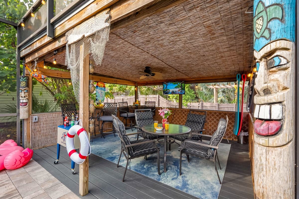 A tropical-themed covered patio featuring tiki décor, string lights, and multiple seating areas beside the pool.
