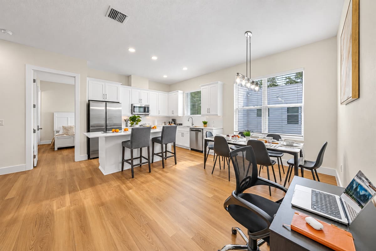 Cook, dine, work, all on one bright floor. The kitchen, dining table, island stools, and a laptop-ready desk share one sunny open space. Remote workers stay connected to the group without losing the ability to focus.