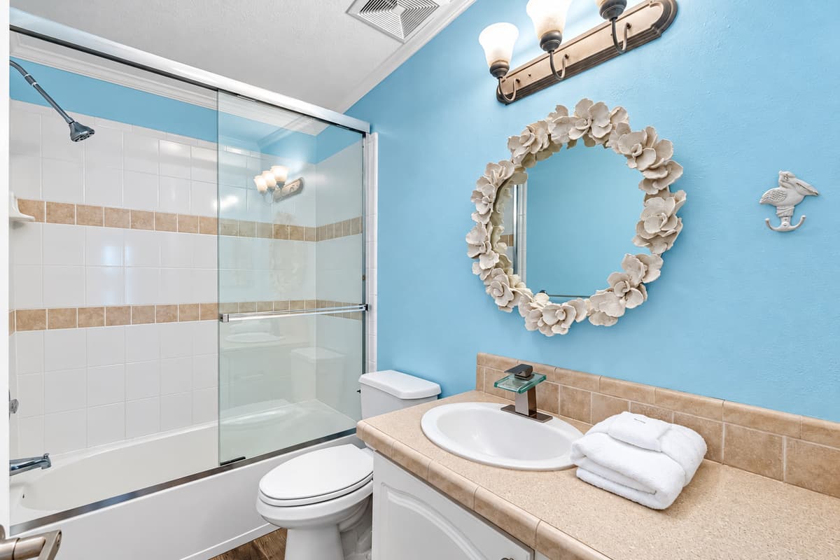 Enjoy a refreshing start to your day in this beautifully maintained bathroom, complete with a full shower and tub, stylish beige tile accents, and a unique flower-framed mirror that adds a touch of personality.