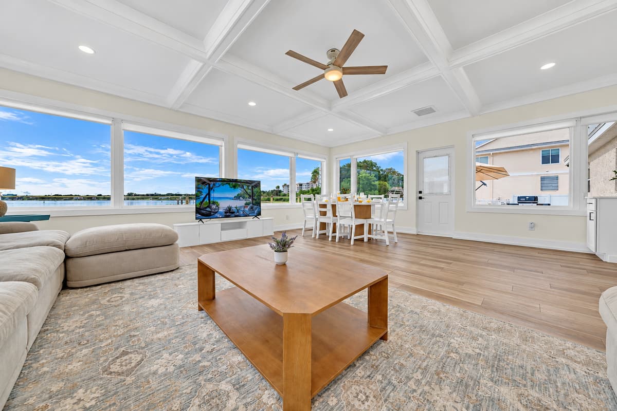 A wide-open waterfront great room. Coffered ceilings, ceiling fans, a big TV and the dining table, all facing the water. One big room where everyone stays together.