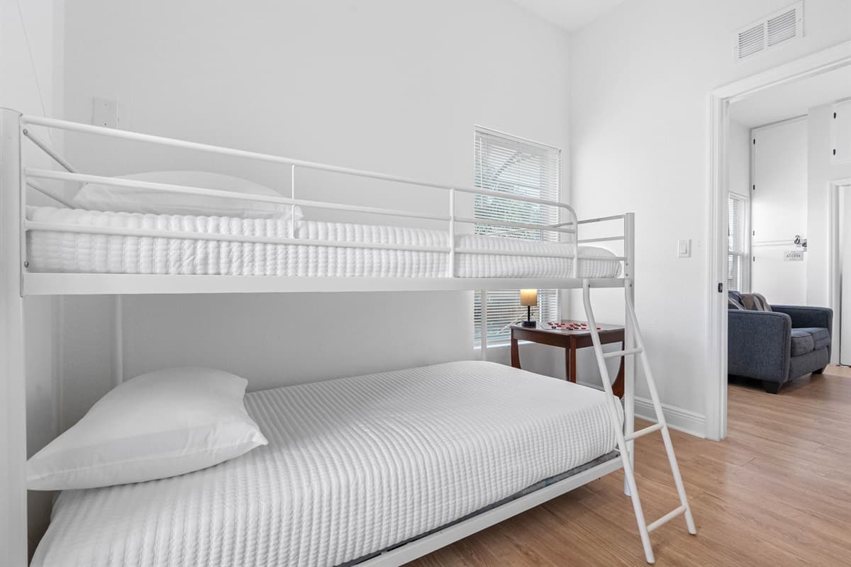 Designed for flexibility and comfort, this bunk room offers two twin beds in a sleek, modern frame. Soft neutral tones, ample natural light, and thoughtful touches like a bedside lamp and game table create a welcoming retreat for younger guests or groups.