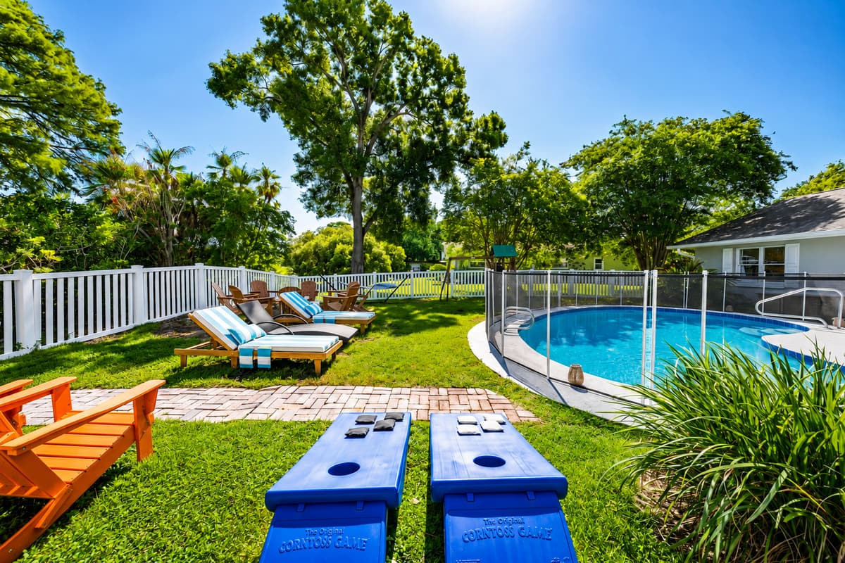 Cornhole set up on the lawn, loungers beside it, pool behind. The yard already has the afternoon figured out.