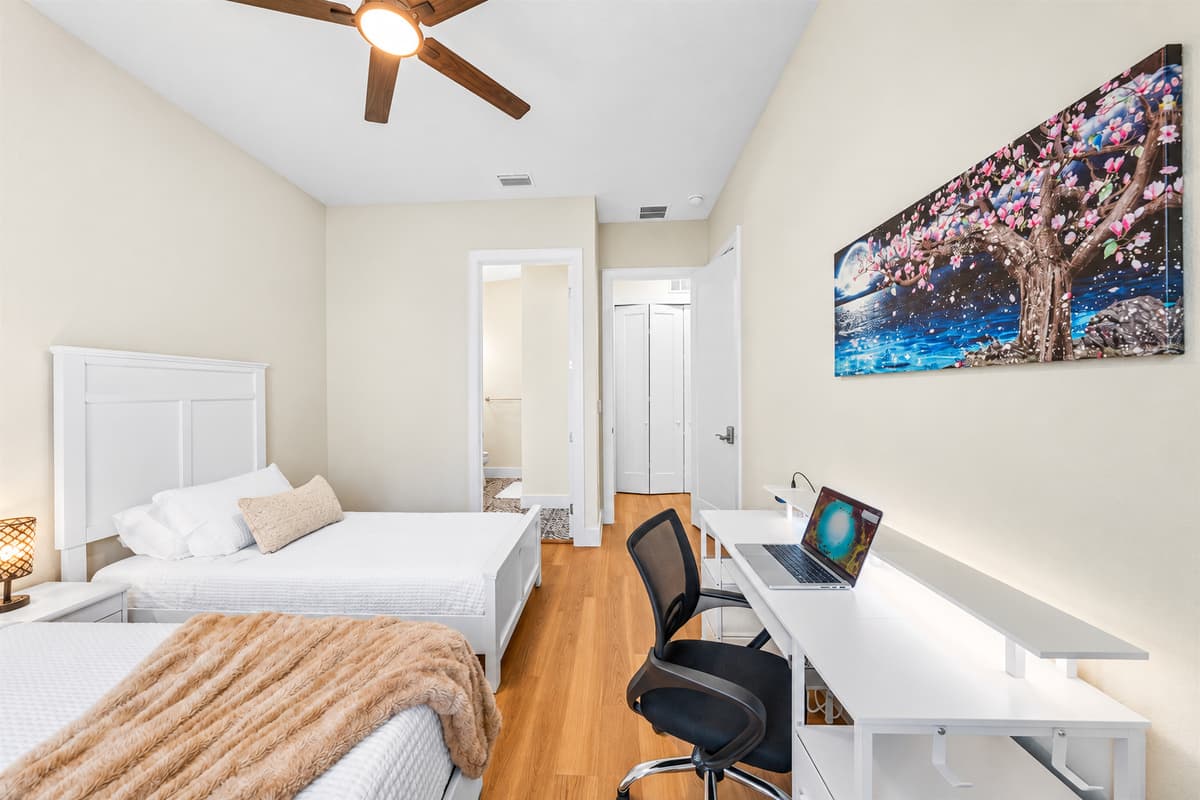 Get work done, then actually rest. A queen bed, a twin, and a long desk under bold tree-of-life art. Remote workers get a real workstation and good light; at night, crisp linens and a ceiling fan pull you into deep sleep.