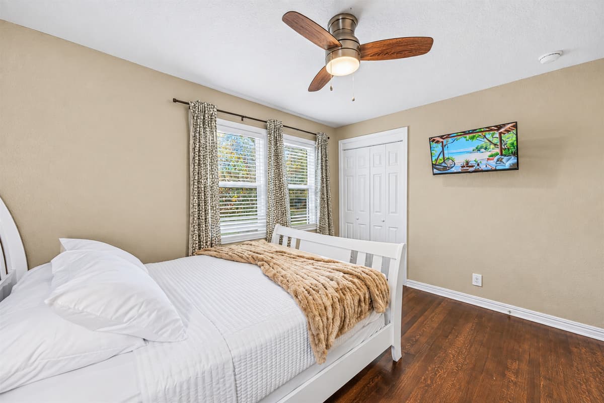 Bright bedroom featuring a comfy bed, wall-mounted TV, and large windows for a relaxing retreat.