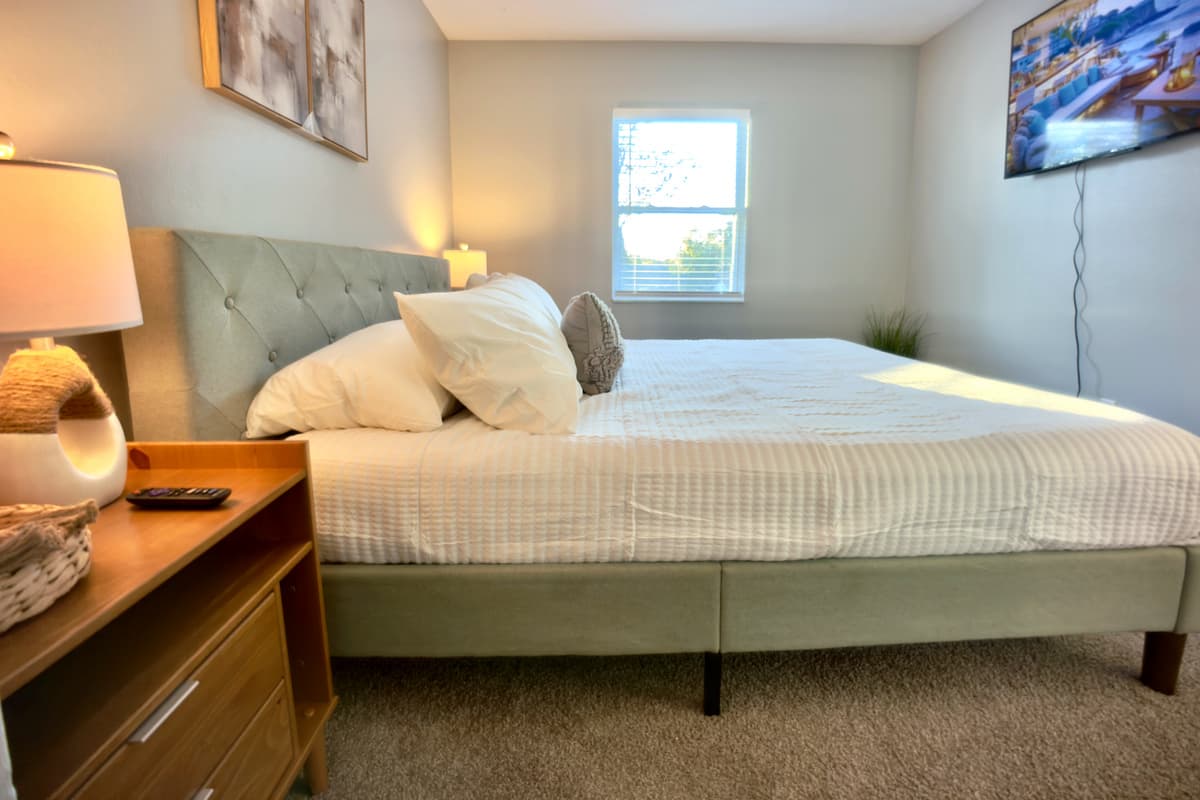 😴 Sweet dreams await in Bedroom 4! This cozy retreat features a plush queen-size bed, stylish nightstand with lamp, flat-screen TV, and natural light — everything for a restful night's sleep. 🌙💤