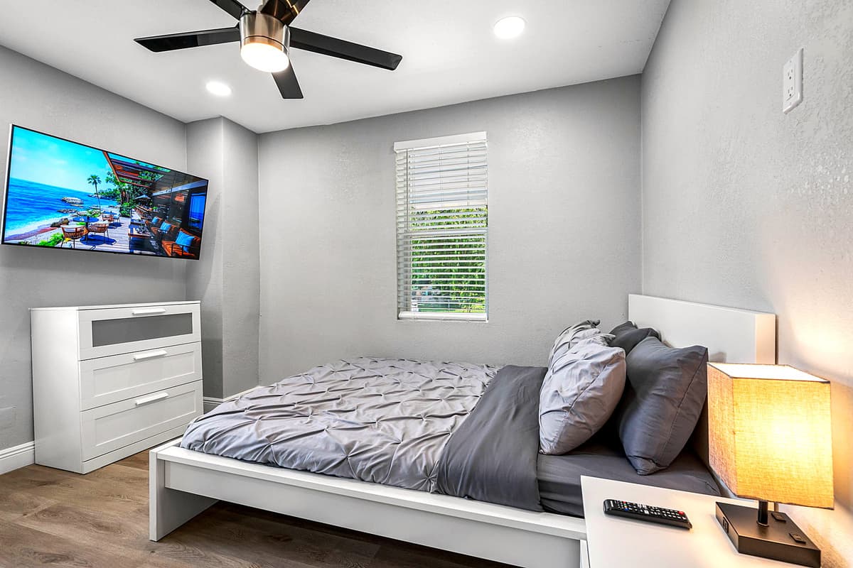 Bedroom 1 — queen bed with fresh linens, wall-mounted TV, nightstands, and a ceiling fan for a restful night's sleep.