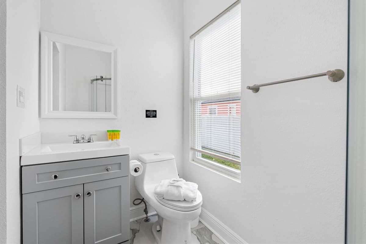 Enjoy the convenience of a private bathroom featuring a glass shower enclosure, smooth countertop sink, framed mirror, and bright natural lighting.