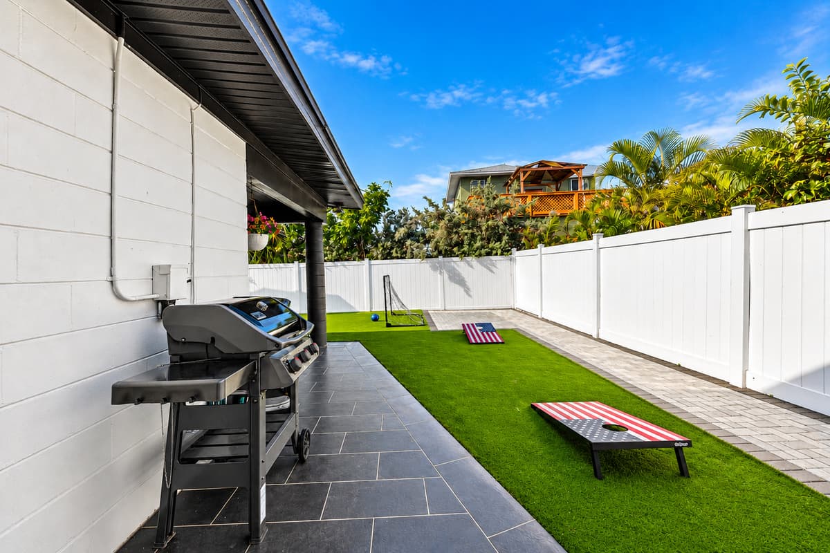 Outdoor grilling station with paved side yard and backyard lawn game setup.