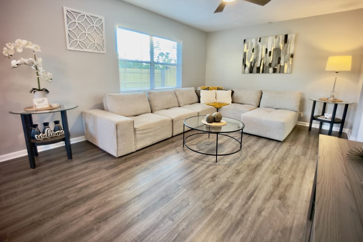 ☀️ Sun-filled and serene! This airy living room is flooded with natural light and features a plush sectional sofa, elegant décor, and hardwood floors — your home away from home! 🏡💛