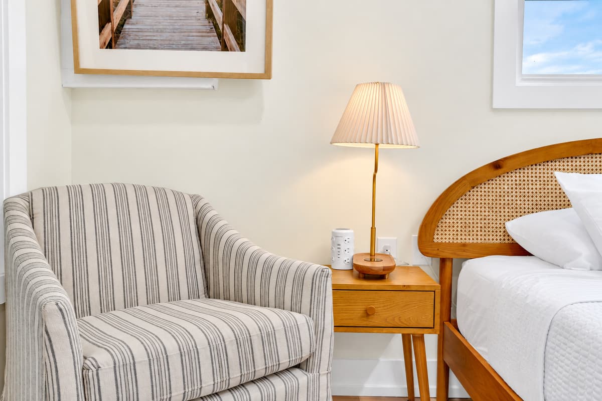 A reading chair, a lamp and calm. A striped armchair and a woven headboard make this king bedroom feel like a boutique inn. Quiet, comfortable and restful.
