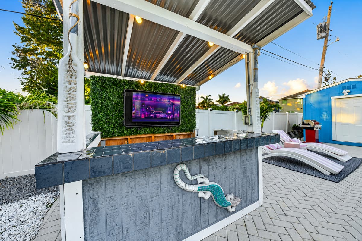 Outdoor bar and entertainment area with a mounted TV, covered seating, and resort-style amenities for relaxing poolside.