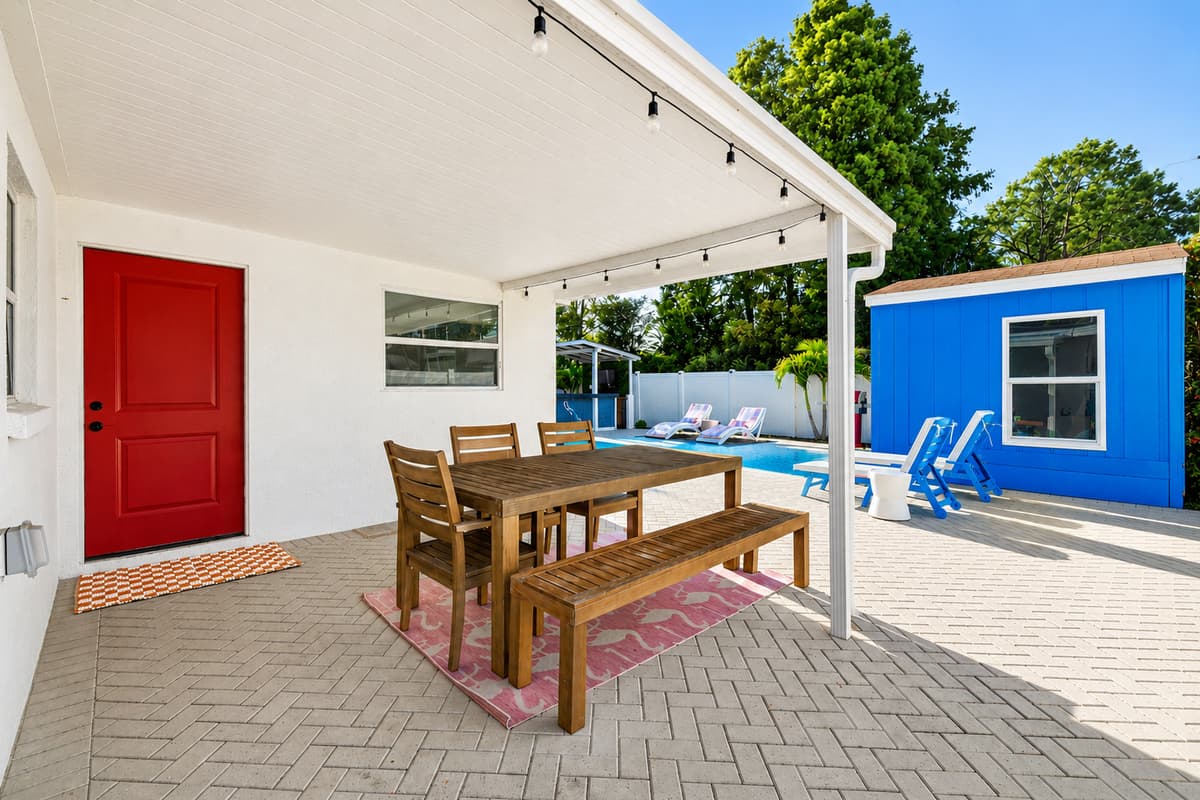 Backyard entertaining area featuring covered patio seating, a bright red accent door, lounge chairs, and easy access to the pool.