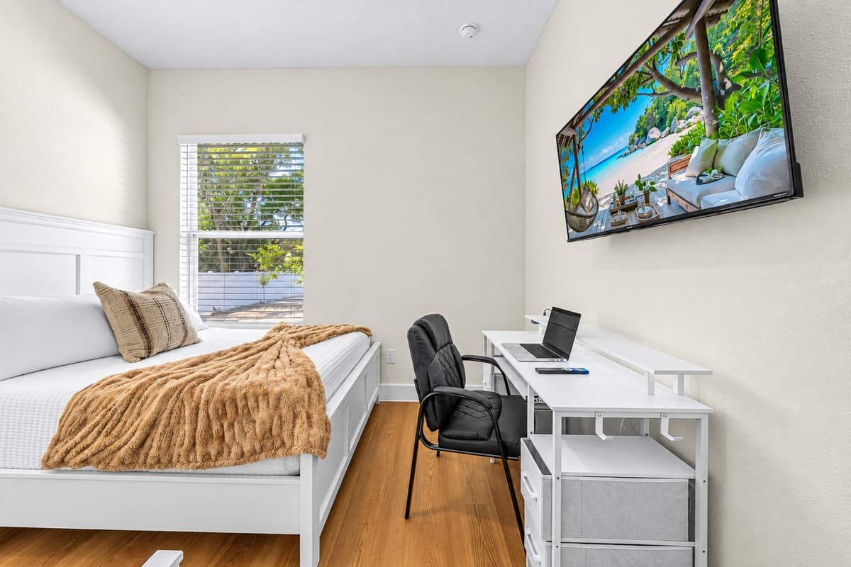 Bright bedroom with comfortable bed, wall-mounted TV, and dedicated workspace.
