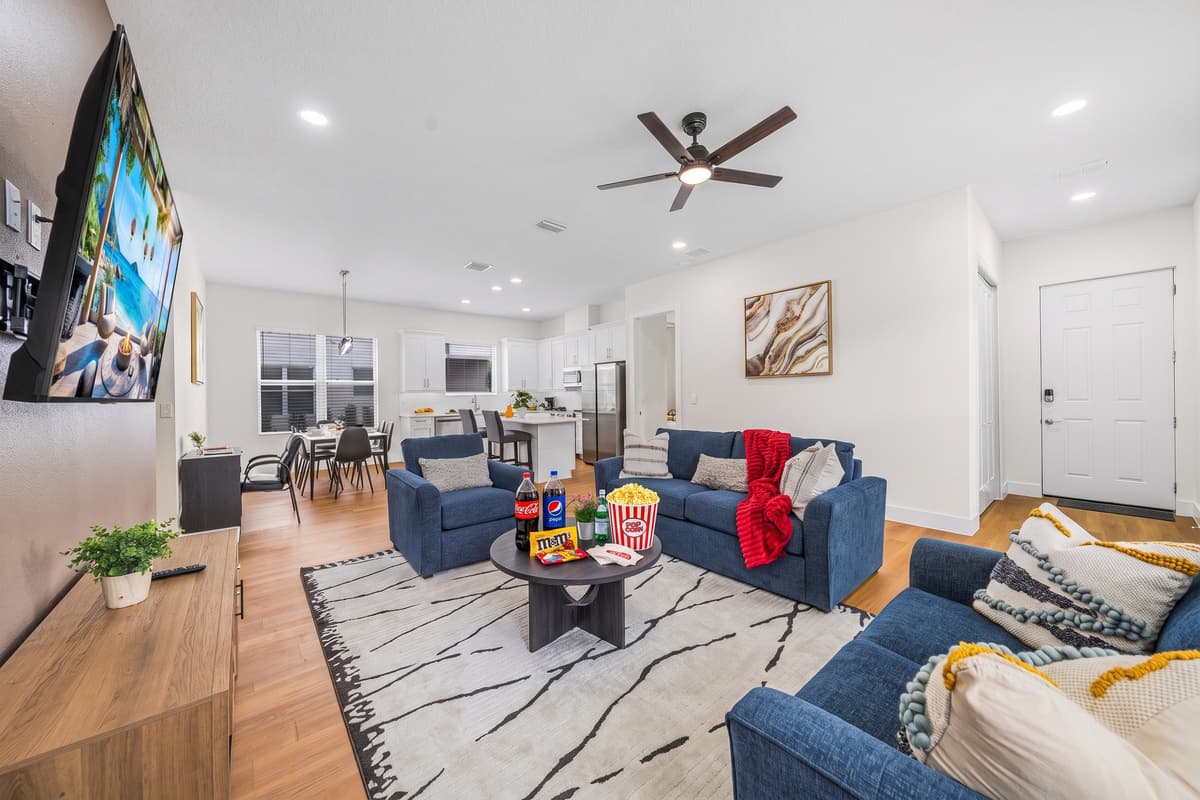 Open living room with group seating, a smart TV, ceiling fans, and views into the kitchen and dining area.