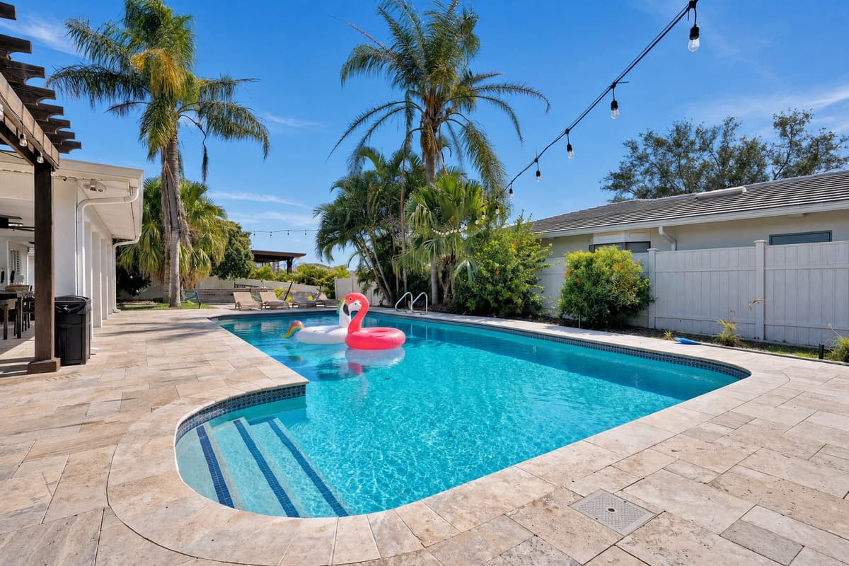 Sunlit pool with a floating flamingo and travertine pavers underfoot, the kind of scene that sells the vacation before guests even arrive