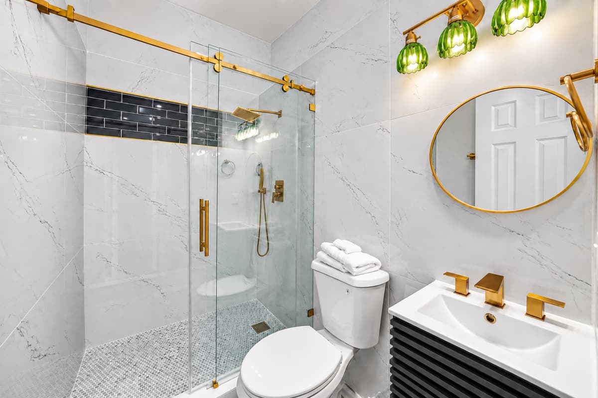 Beautifully renovated bathroom featuring a spacious glass-enclosed shower, modern gold accents, and upscale finishes.