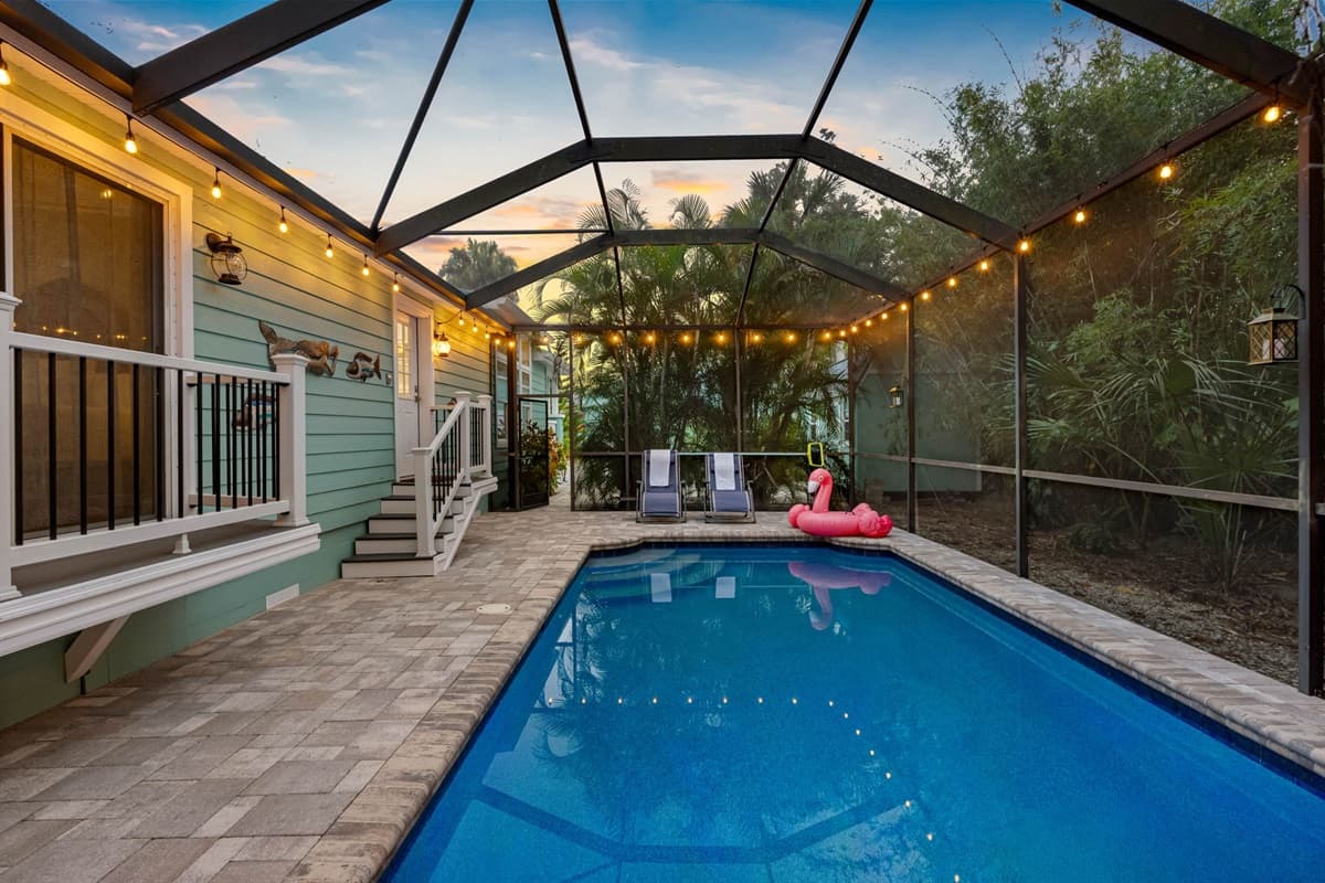 A sparkling screened-in pool surrounded by tropical greenery and twinkling string lights, perfect for day or night relaxation.