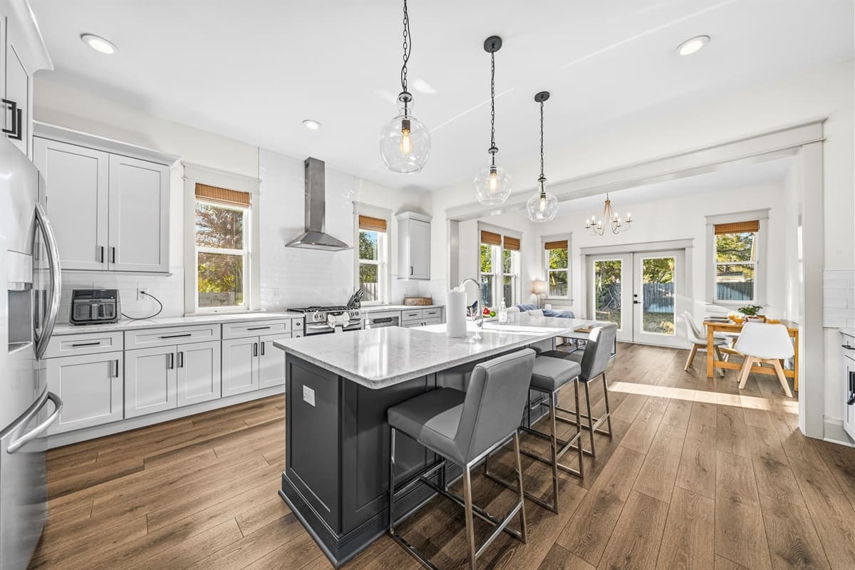 The kitchen island with sleek bar stools, statement pendant lighting, and French doors opening to the back patio — perfect for cooking, entertaining, and indoor-outdoor living in this brand-new Seminole Heights home.
