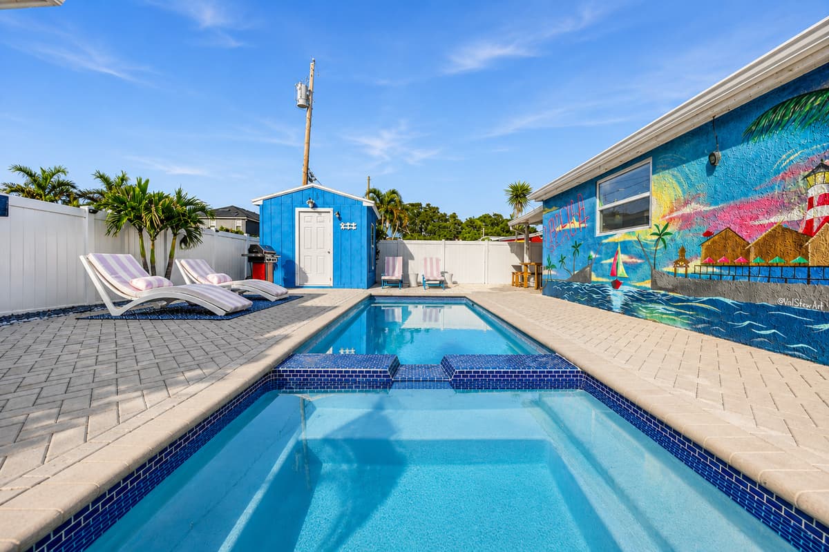 Private rectangular swimming pool with built-in spa section, lounge chairs, paver deck, and vibrant flamingo-themed mural along the exterior wall.