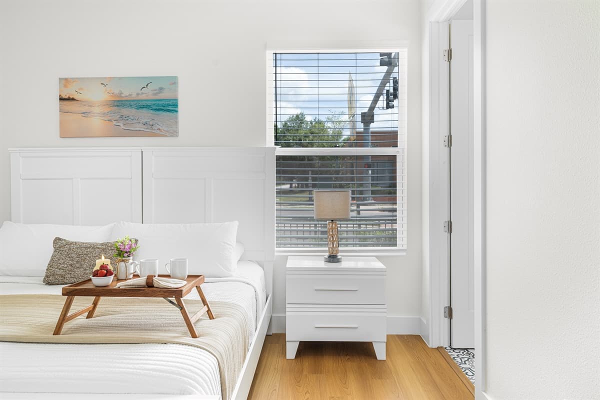 Retreat to a serene bedroom with crisp white linens, a bedside reading tray, and artwork for a hotel-like feel.