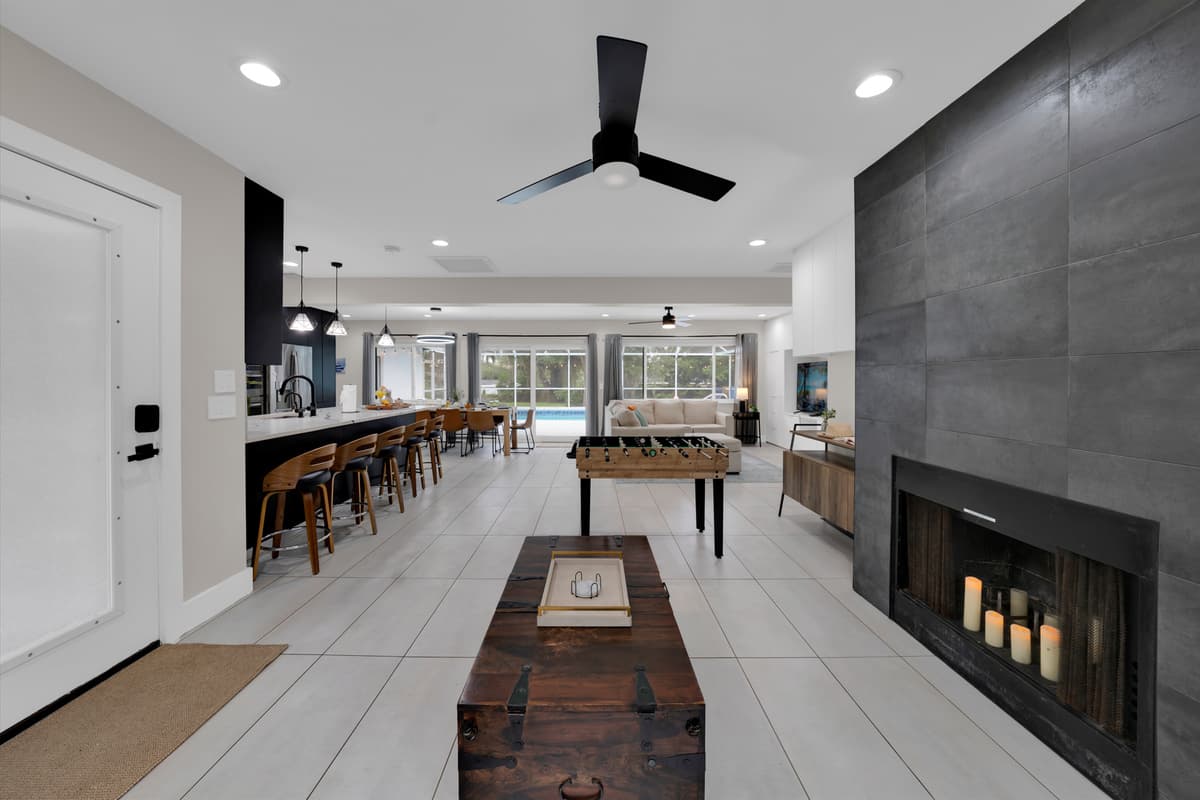 Relax by the fireplace in a beautifully designed space where every detail flows together, from the cozy living room to the dining area, kitchen, and pool beyond.