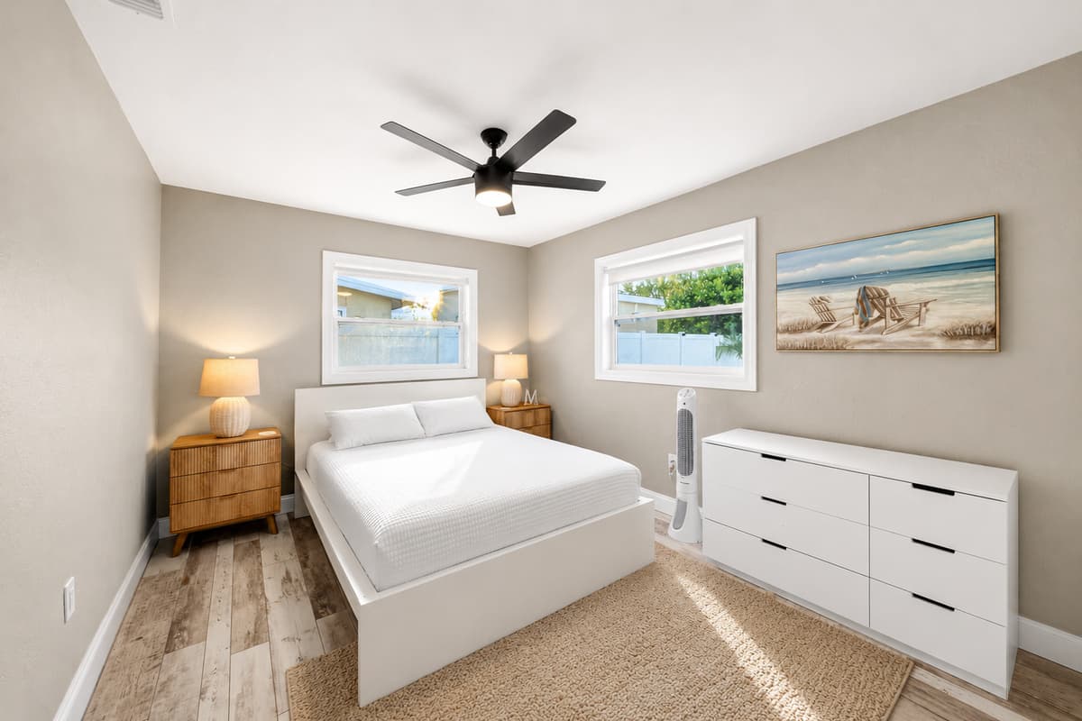 Bright and inviting bedroom with modern furnishings, beach-themed artwork, ceiling fan, and ample storage.