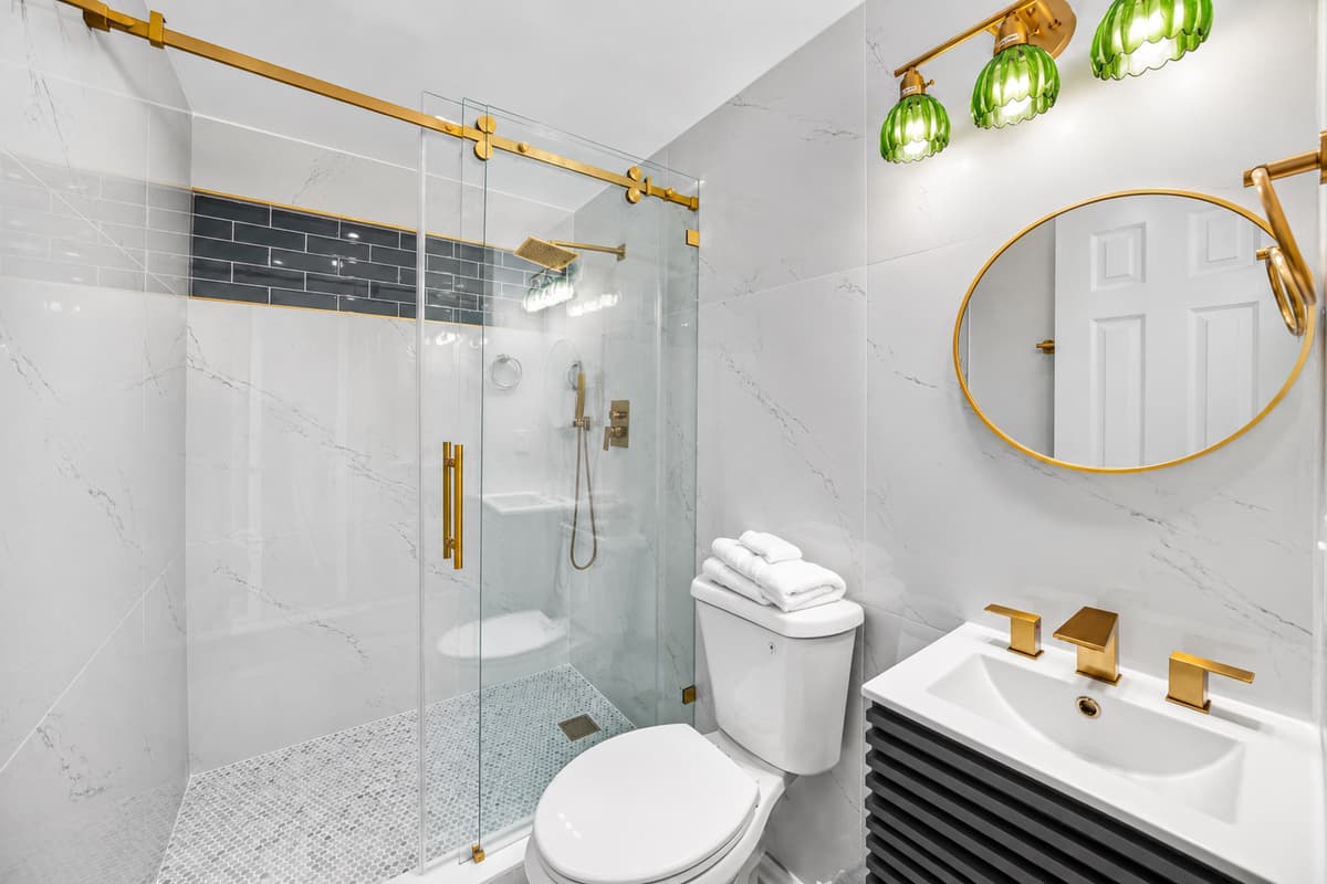 Beautifully renovated bathroom featuring a spacious glass-enclosed shower, modern gold accents, and upscale finishes.