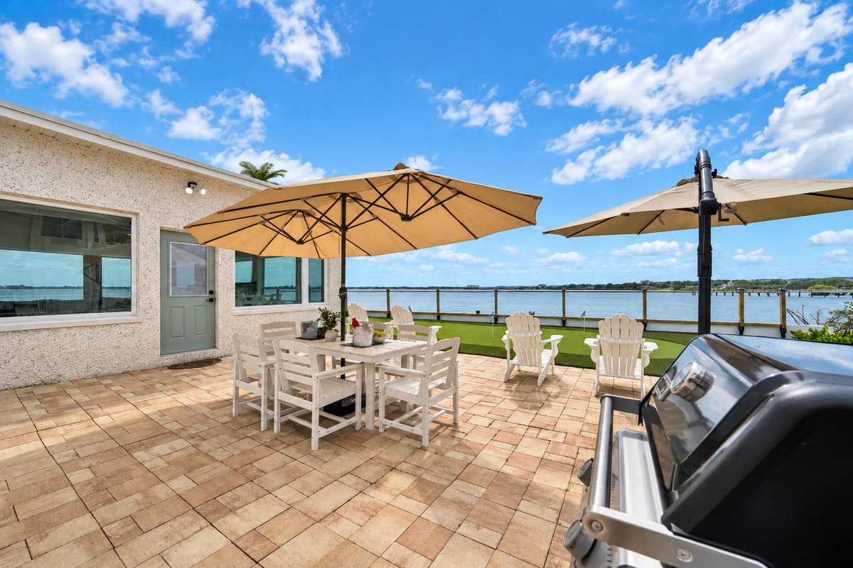 Grill fired up, table set, bay waiting. A gas grill, a big patio table under umbrellas and a view of the water. Dinner outside is the obvious choice here.