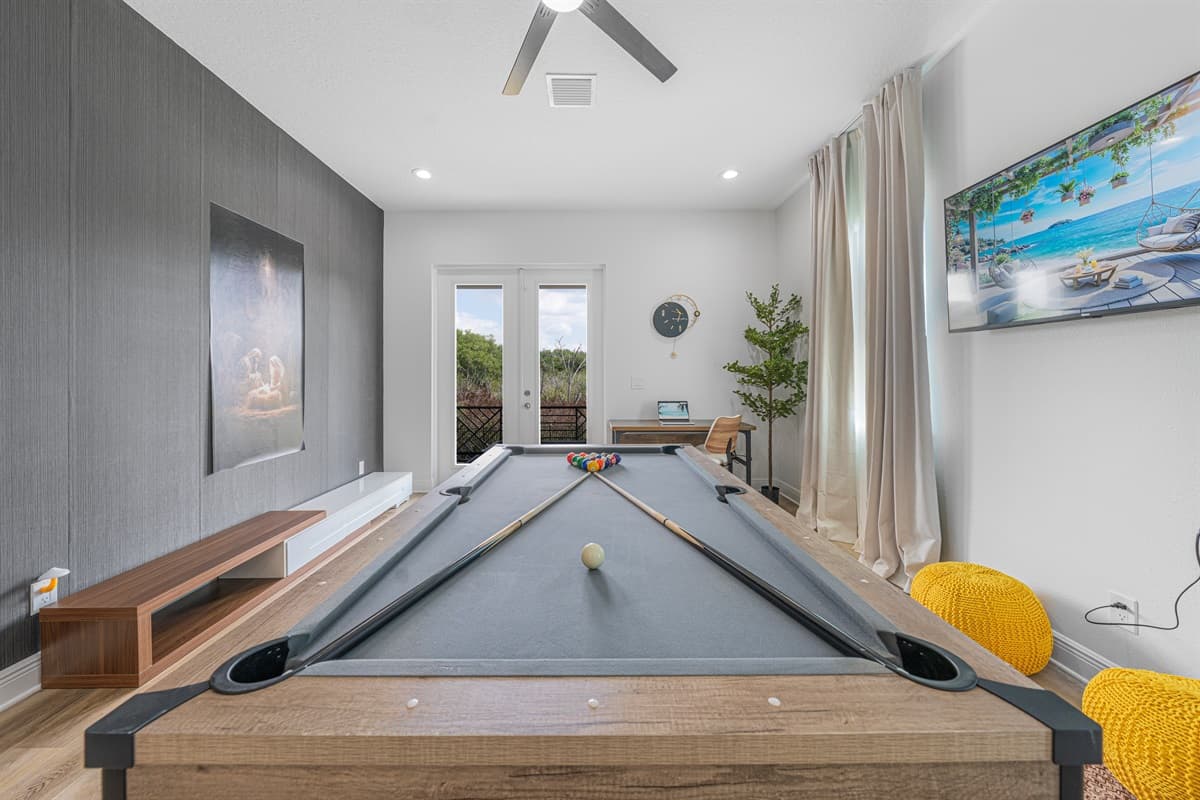 Full view of the game room highlighting the pool table, large TV, and open layout with natural light.
