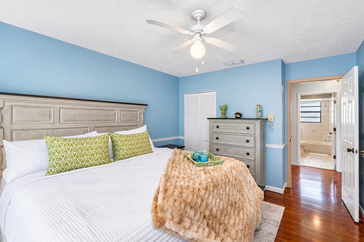 With its coastal-inspired tones, plush bedding, and fresh green accents, this bedroom is a soothing escape just steps from the bath.