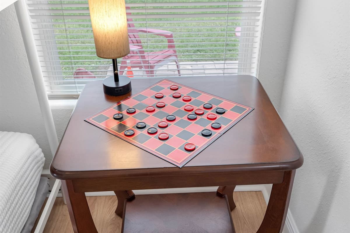 This bunk bedroom is ideal for kids or additional guests. It features sturdy twin-over-twin bunk beds with crisp white linens, warm wood flooring, and natural light from a large window. A cozy game table adds a playful touch.