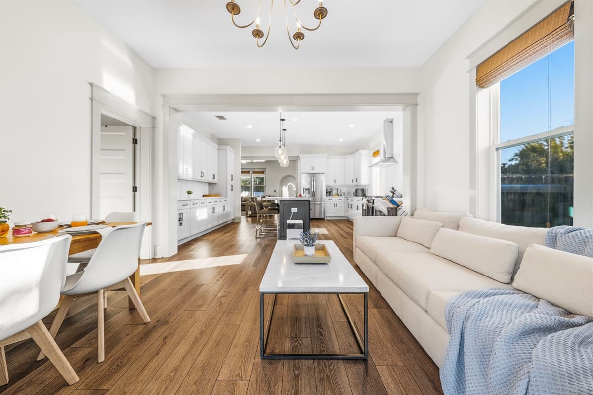 Sweeping view of the open-concept living and dining area — gold chandelier, cream sofa, farmhouse dining table, French doors, and incredible natural light throughout. Brand-new construction designed to impress in Seminole Heights.
