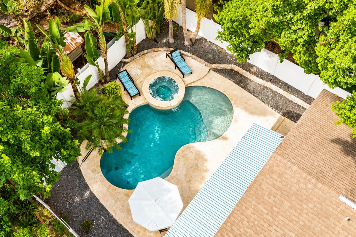 Take in a bird's-eye view of your private tropical oasis featuring a resort-style pool, attached spa, and lush landscaping.