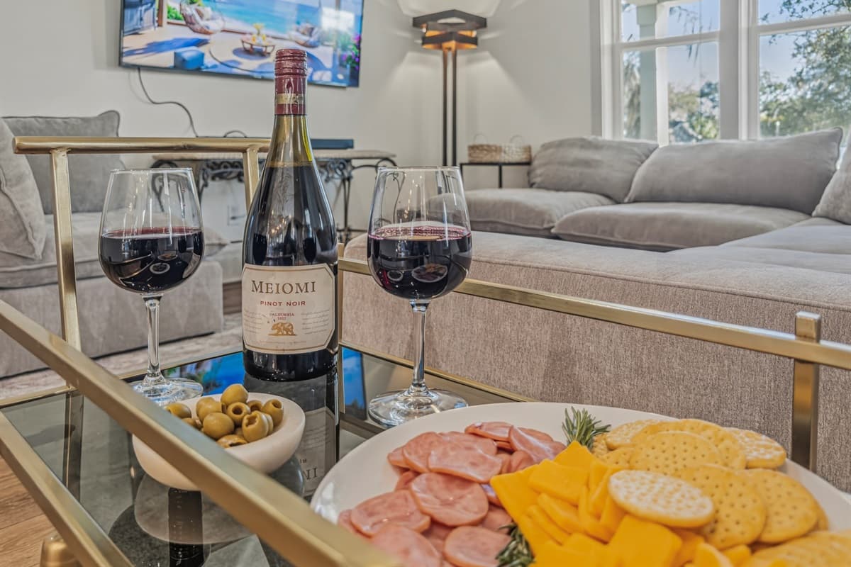 Entertain in style — the living room coffee table set with a bottle of red wine, charcuterie, olives, and crackers. This brand-new Seminole Heights home is made for making lasting memories with great company.