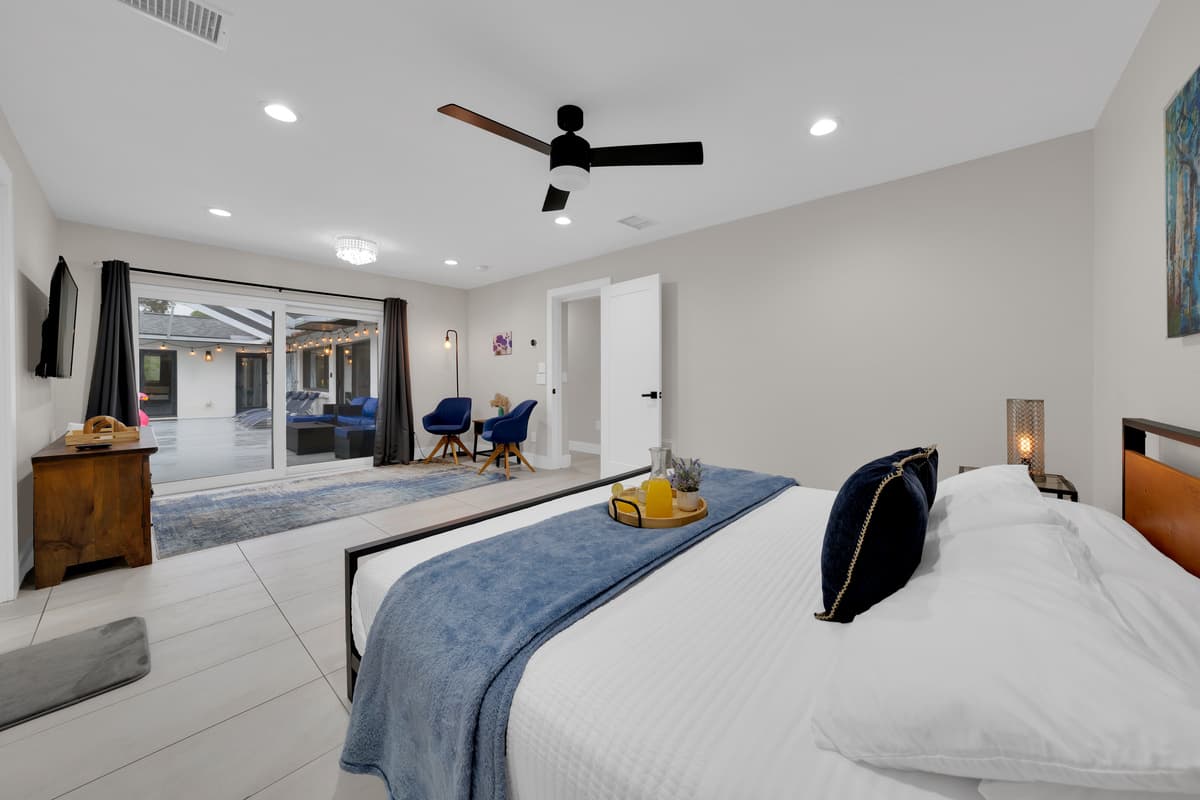 Bed dressed in white and navy, a breakfast tray waiting, and a sliding door open straight to the pool area, this room doesn't separate rest from view.