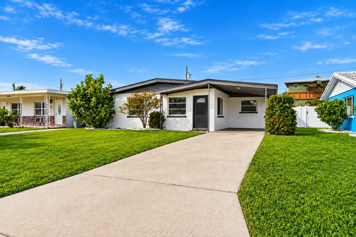 Full exterior view of the property with large driveway, covered parking, and tropical curb appeal.