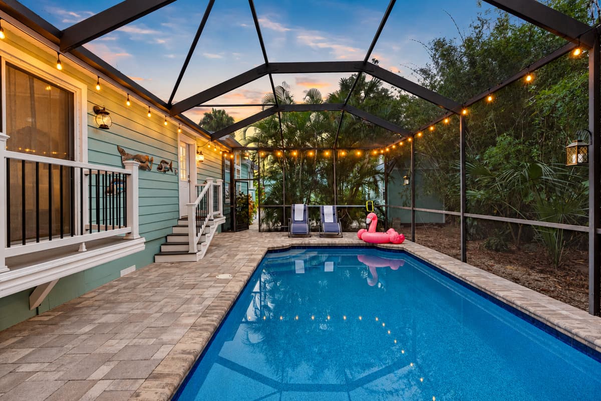 A sparkling screened-in pool surrounded by tropical greenery and twinkling string lights, perfect for day or night relaxation.