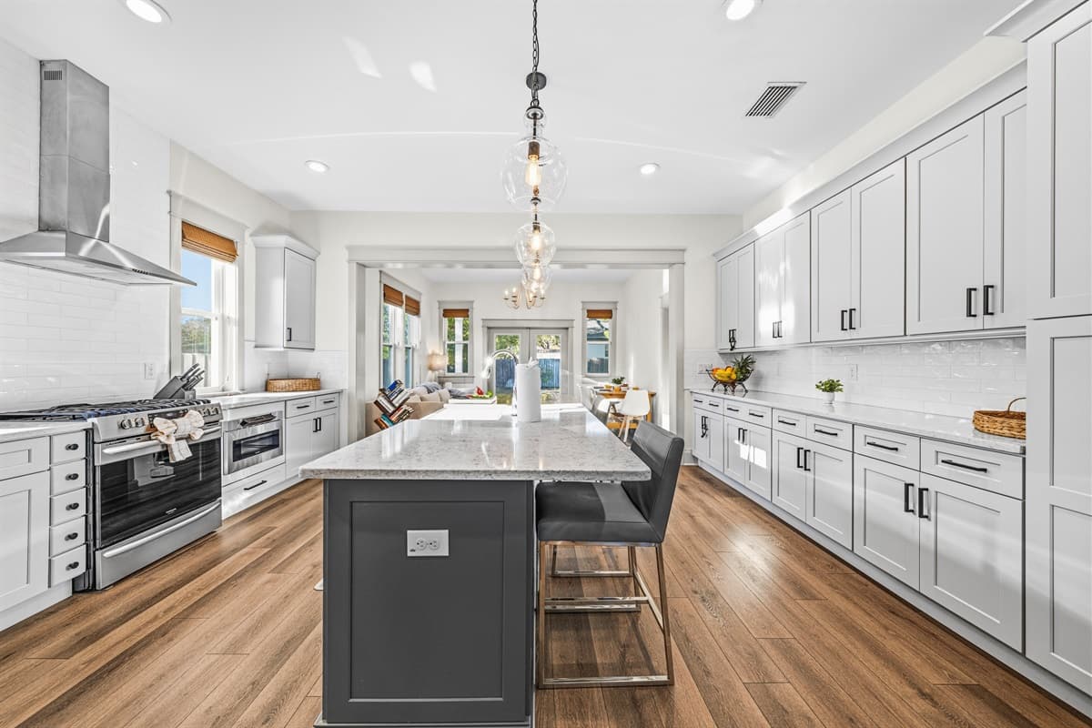 Chef's dream kitchen! Brand-new with floor-to-ceiling white shaker cabinets, a dark center island, elegant pendant lights, stainless steel appliances, and a pro-grade range hood — all on rich hardwood floors.