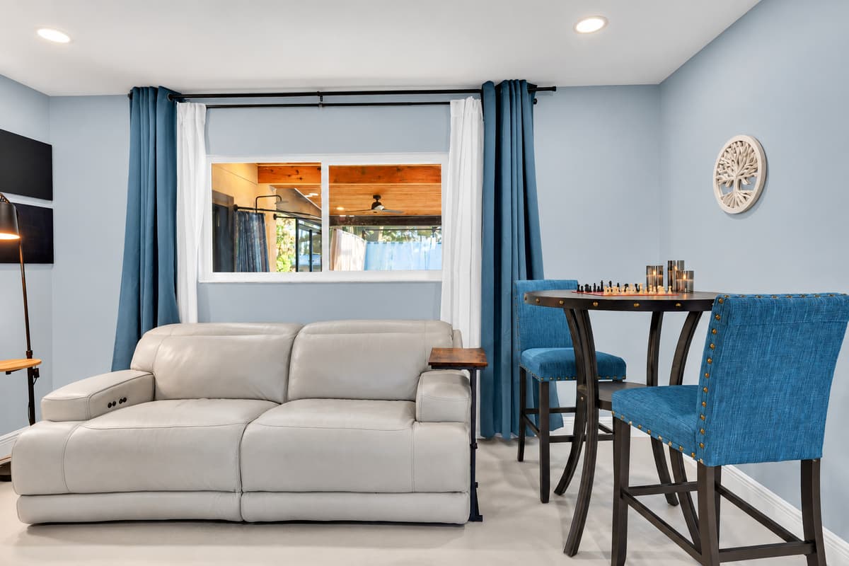 Quiet corner, cold air, coffee within reach. Recliner-style sofa, a small table by the window and light through the blinds — the spot for the person who wakes up first.