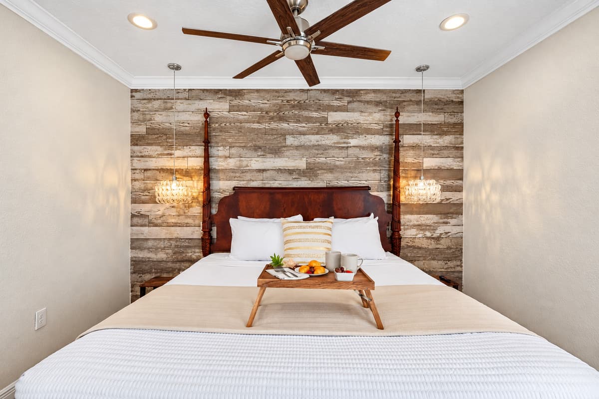 The wood-paneled accent wall and rich four-poster bed bring warmth and character, complemented by neutral tones and polished tile floors.