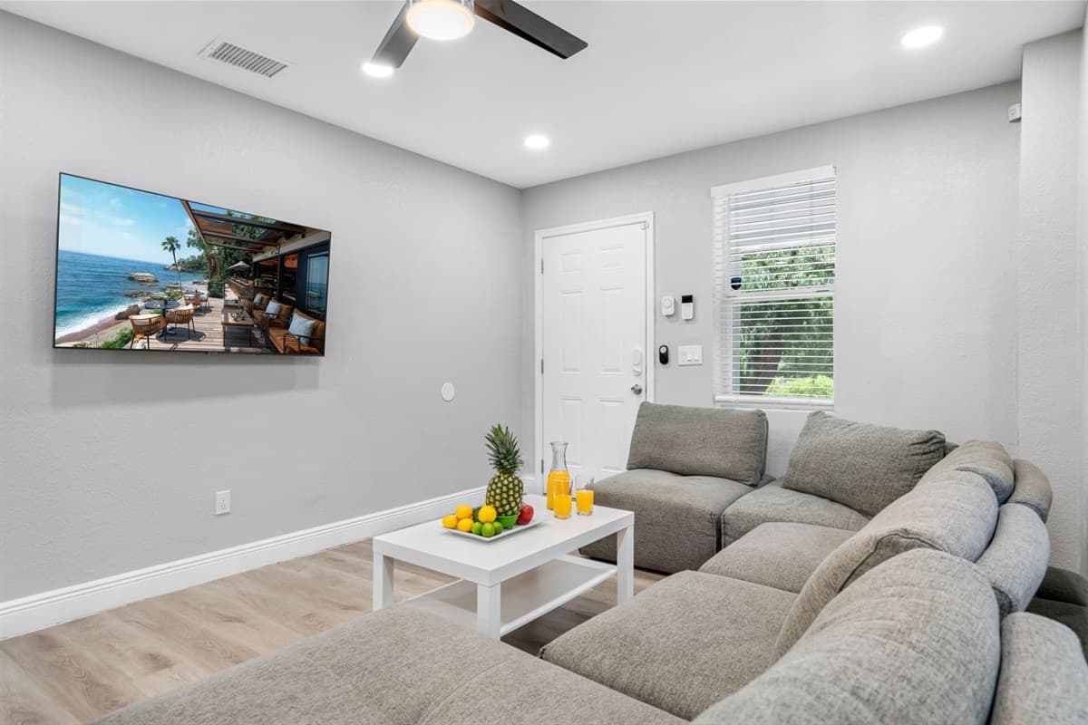 Living room with wall-mounted flat-screen TV, natural light, and modern ceiling fan.