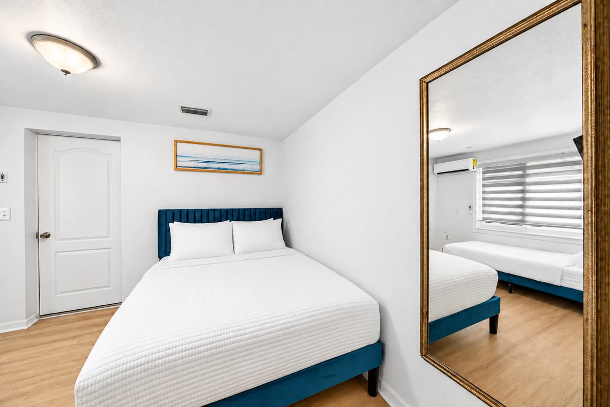 Bright and inviting guest bedroom featuring a comfortable queen bed, stylish furnishings, and a large mirror that enhances the spacious feel of the room.