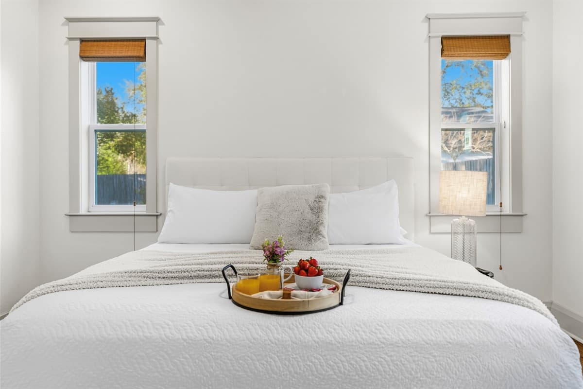 Wake up to pure bliss — crisp white bedding, a wooden breakfast tray with fresh fruit, and twin windows overlooking the lush Seminole Heights greenery. Brand-new construction comfort that feels like a boutique hotel.