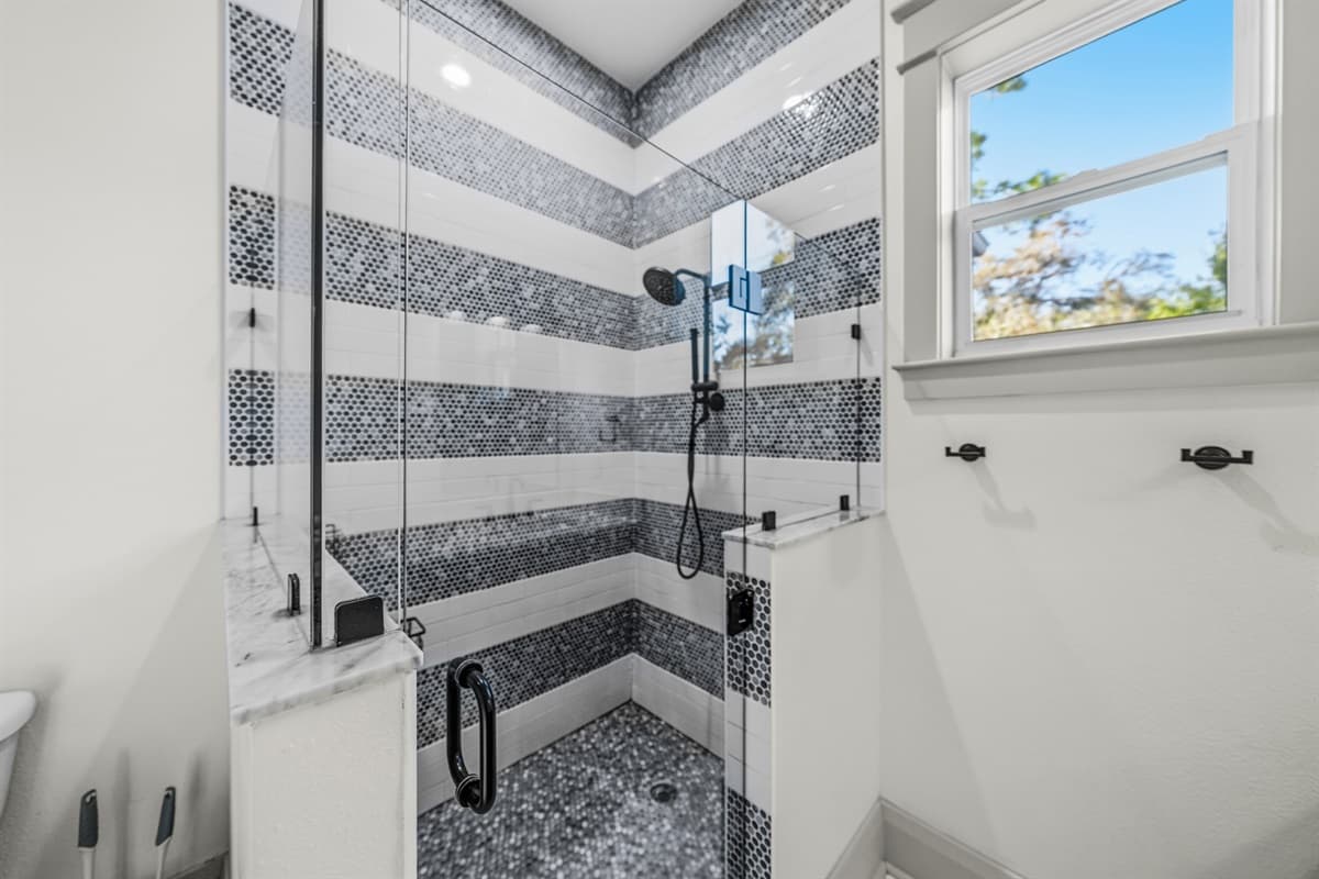Showstopper walk-in shower with floor-to-ceiling blue and white herringbone mosaic tile, glass door, and a large window framing the Florida blue sky. Brand-new construction luxury at its absolute finest.