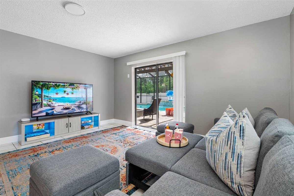 The centerpiece of the room is a modern gray sectional couch, plush and roomy, complete with a pair of matching ottomans for extra legroom or casual seating.
