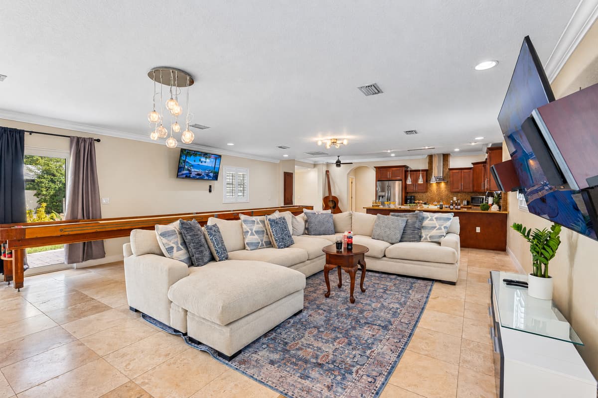 Designed for socializing, this open-concept living room offers a spacious sectional, a shuffleboard table for friendly competition, and dual flat-screen TVs for immersive entertainment.