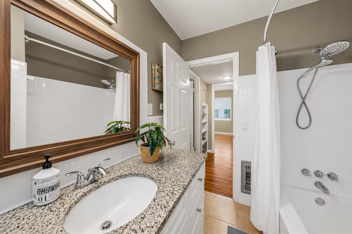 Clean and inviting second bathroom with granite countertops, framed mirror, and shower/tub combination.